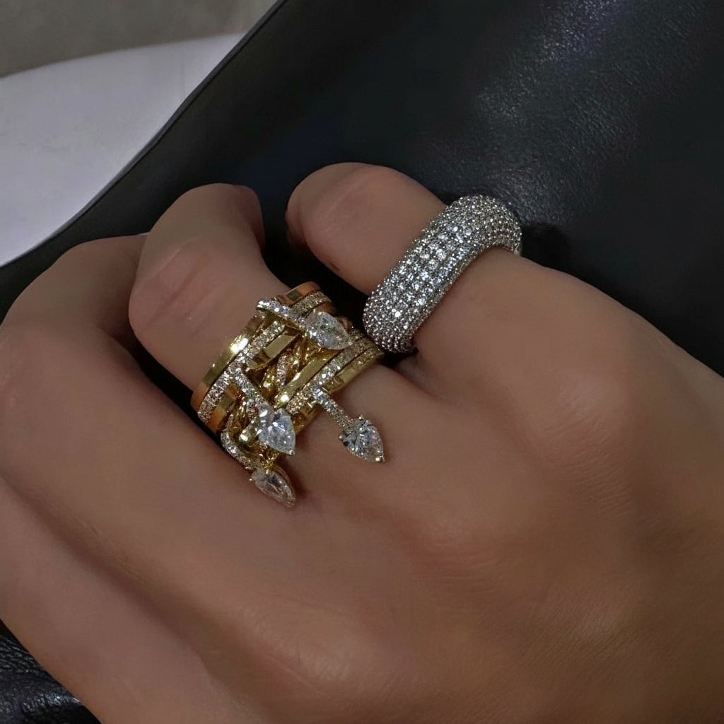 Close-up of a hand wearing two gold rings with gemstones on a dark background.