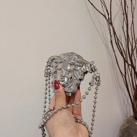 Silver chain bag held by a hand with red nail polish against a neutral background