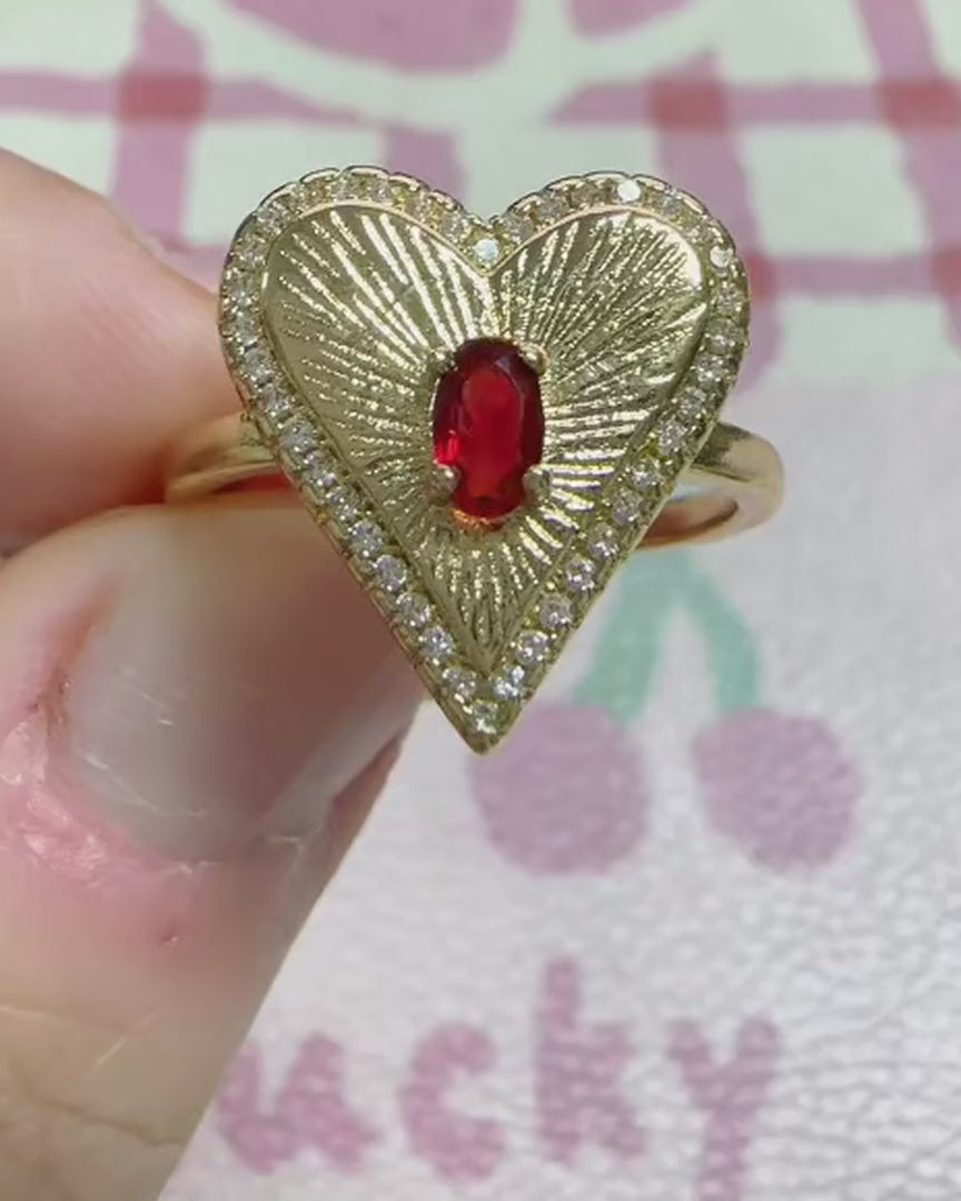 Gold heart cocktail ring with red stone and crystal pavé border, shown on hand