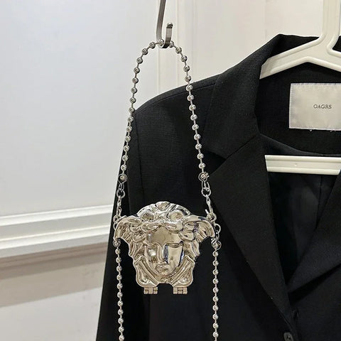 Silver chain bag with Medusa head design hanging on a black jacket.